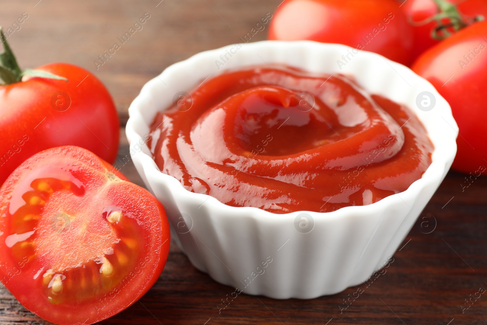 Photo of Bowl of tasty ketchup and tomatoes on wooden table, closeup