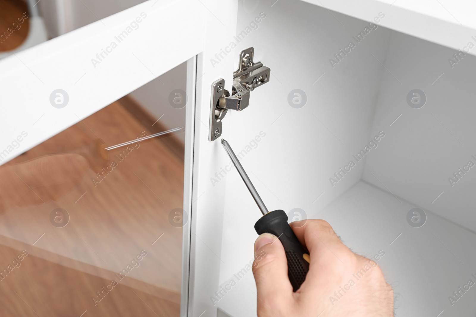 Photo of Man fixing door angle hinge of wooden cabinet, closeup view