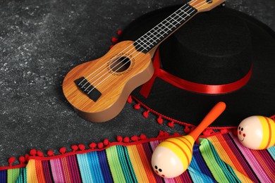 Black Flamenco hat, ukulele, poncho and maracas on dark textured table, closeup