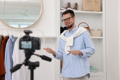 Photo of Smiling fashion blogger showing clothes while recording video at home