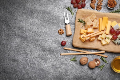 Cheese plate with honey, grapes and nuts on grey table, flat lay. Space for text