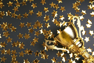 Gold trophy cup and confetti on black background, flat lay. Space for text