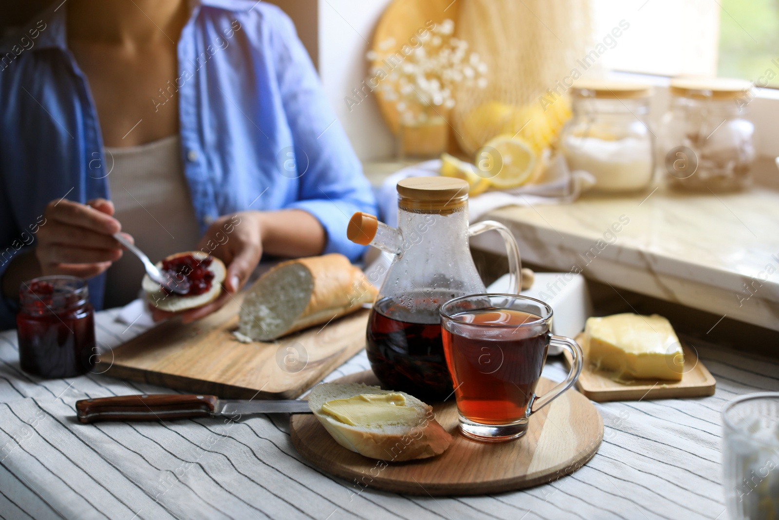 Photo of Woman spreading jam onto bread at table indoors, focus on aromatic tea