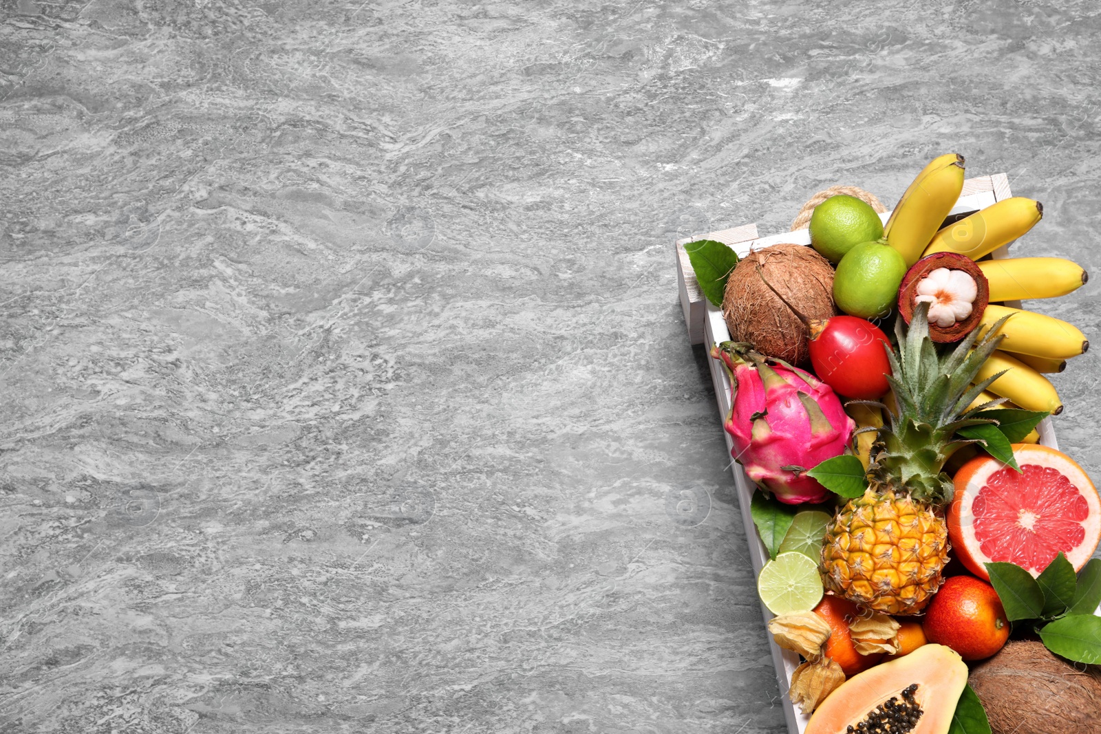 Photo of Different tropical fruits in wooden box on grey background, top view. Space for text