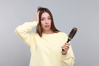 Photo of Emotional woman holding brush with lost hair on light grey background. Alopecia problem