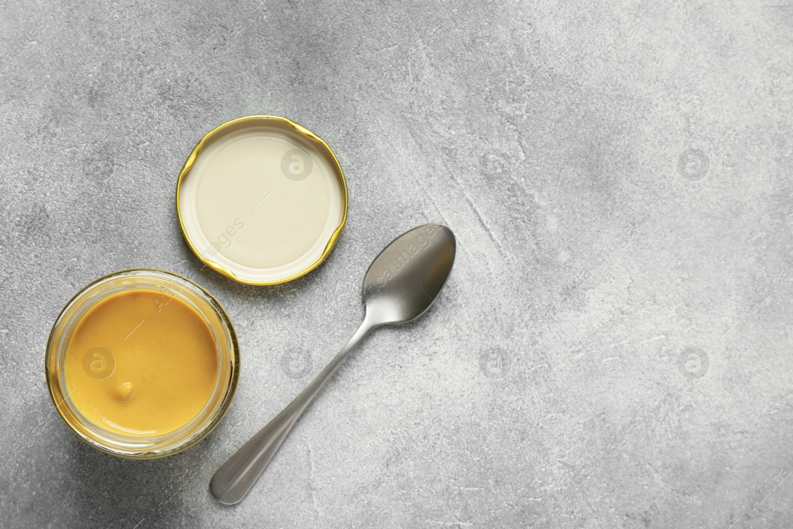 Photo of Spicy mustard in glass jar and spoon on grey table, flat lay. Space for text