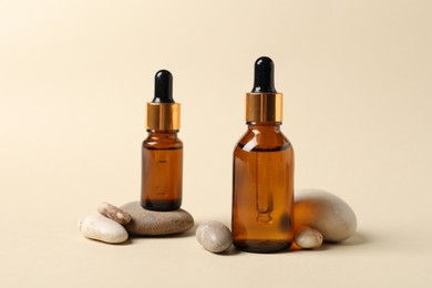 Photo of Bottles of cosmetic serum and stones on beige background