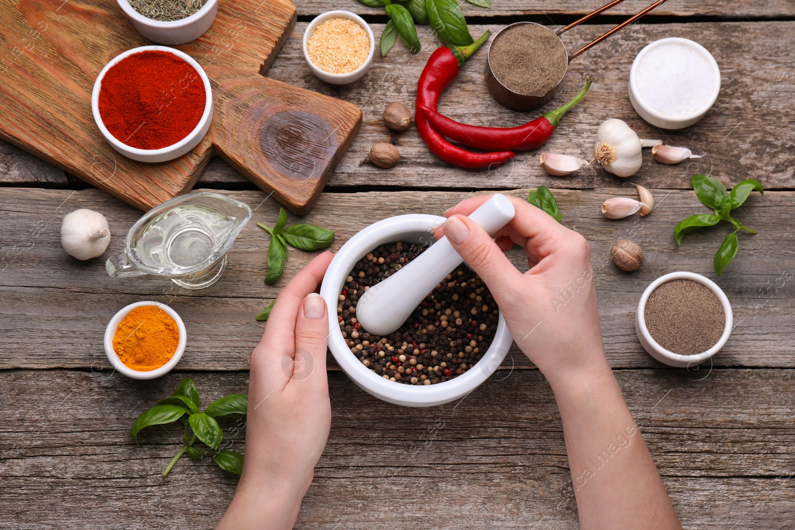 Photo of Woman grinding peppercorns in mortar at wooden table, top view