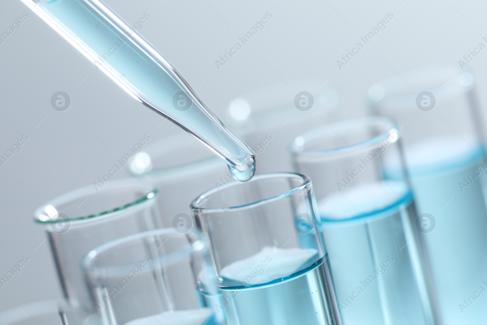 Photo of Dripping liquid from pipette into test tube on light background, closeup