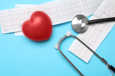 Photo of Cardiogram report, red heart and stethoscope on light blue background, flat lay