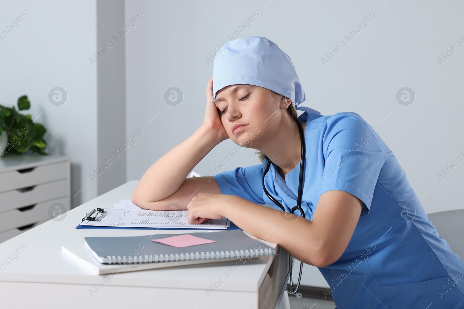 Photo of Tired young doctor sleeping at workplace in office