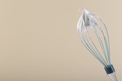 Whisk with whipped cream on beige background. Space for text