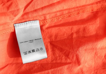 Photo of Clothing label in different languages on orange garment, top view