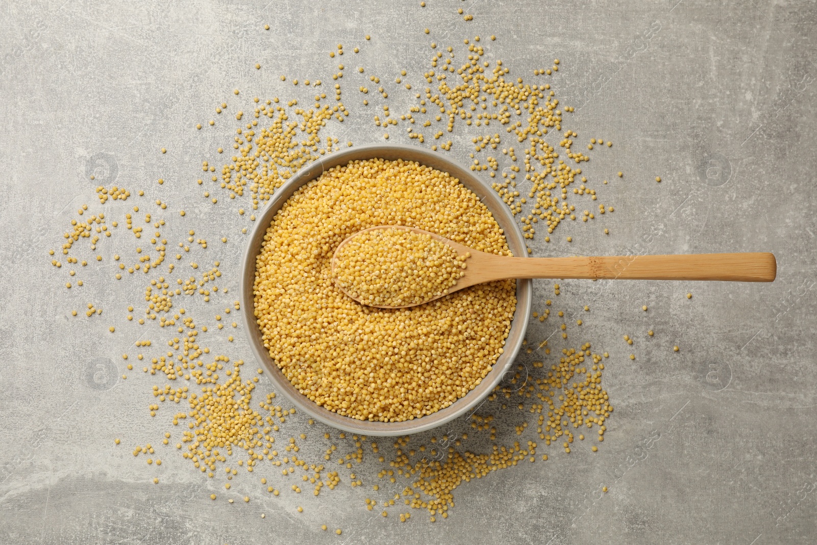 Photo of Millet groats in bowl and spoon on light grey table, top view