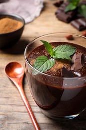 Glass of delicious hot chocolate with fresh mint and spoon on wooden table