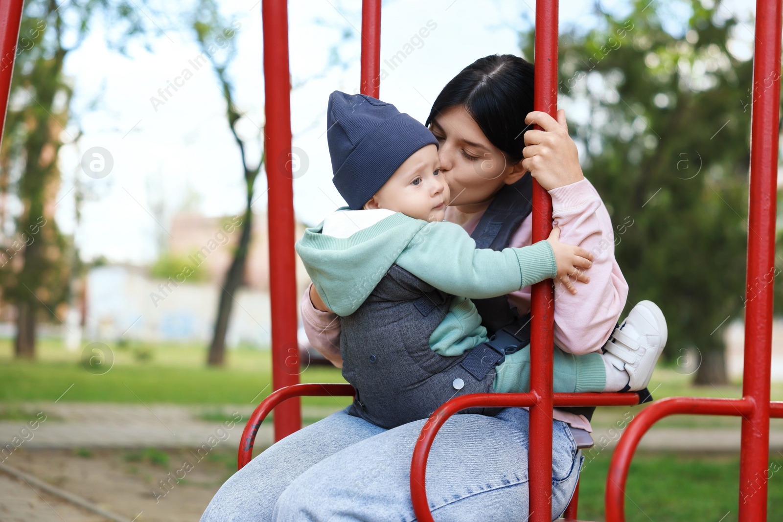 Photo of Mother holding her child in sling (baby carrier) on swing outdoors. Space for text