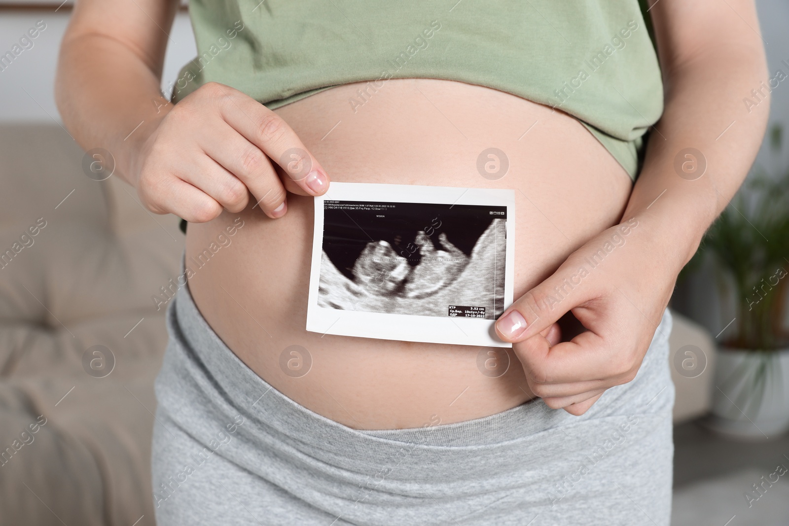 Photo of Pregnant woman with ultrasound picture of baby in living room, closeup