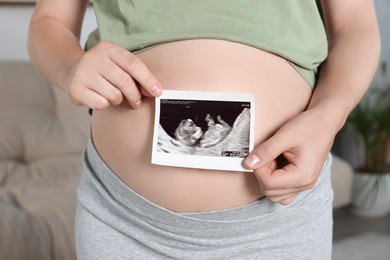 Photo of Pregnant woman with ultrasound picture of baby in living room, closeup