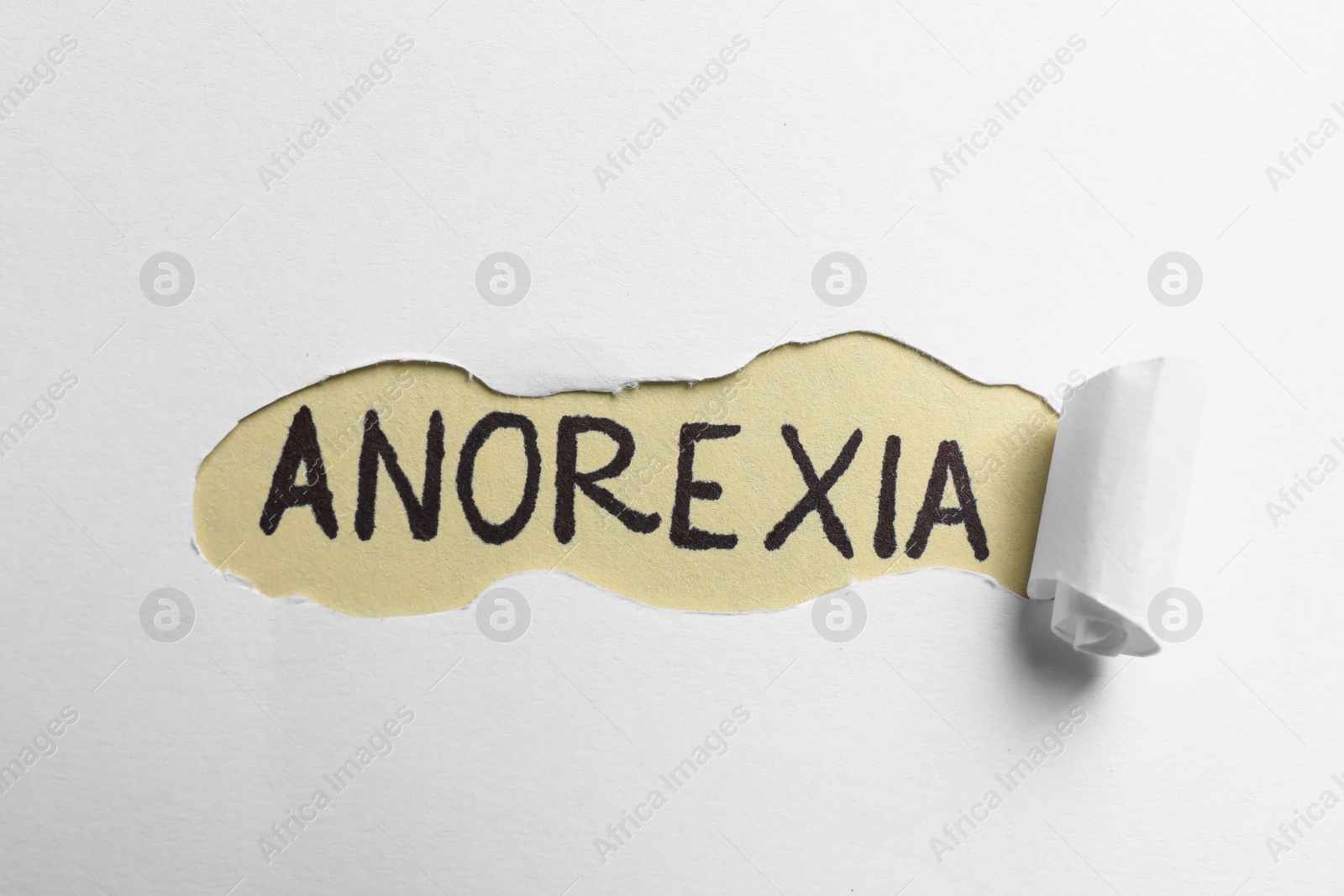 Photo of Word Anorexia written on beige background, view through hole in white paper