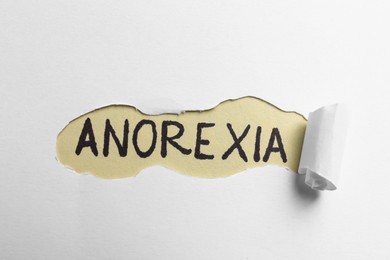Photo of Word Anorexia written on beige background, view through hole in white paper