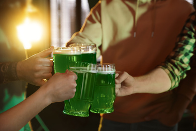 Photo of Group of friends toasting with green beer in pub, closeup. St. Patrick's Day celebration