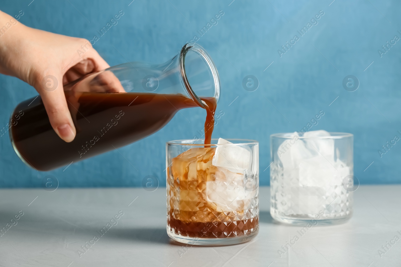 Photo of Woman pouring cold brew coffee into glass on table