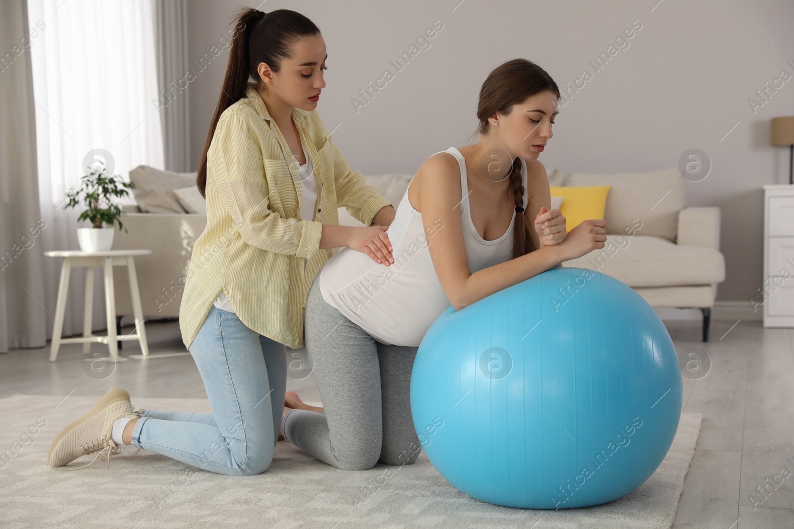 Photo of Doula working with pregnant woman in living room. Preparation for child birth