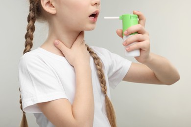 Photo of Little girl using throat spray on light grey background, closeup