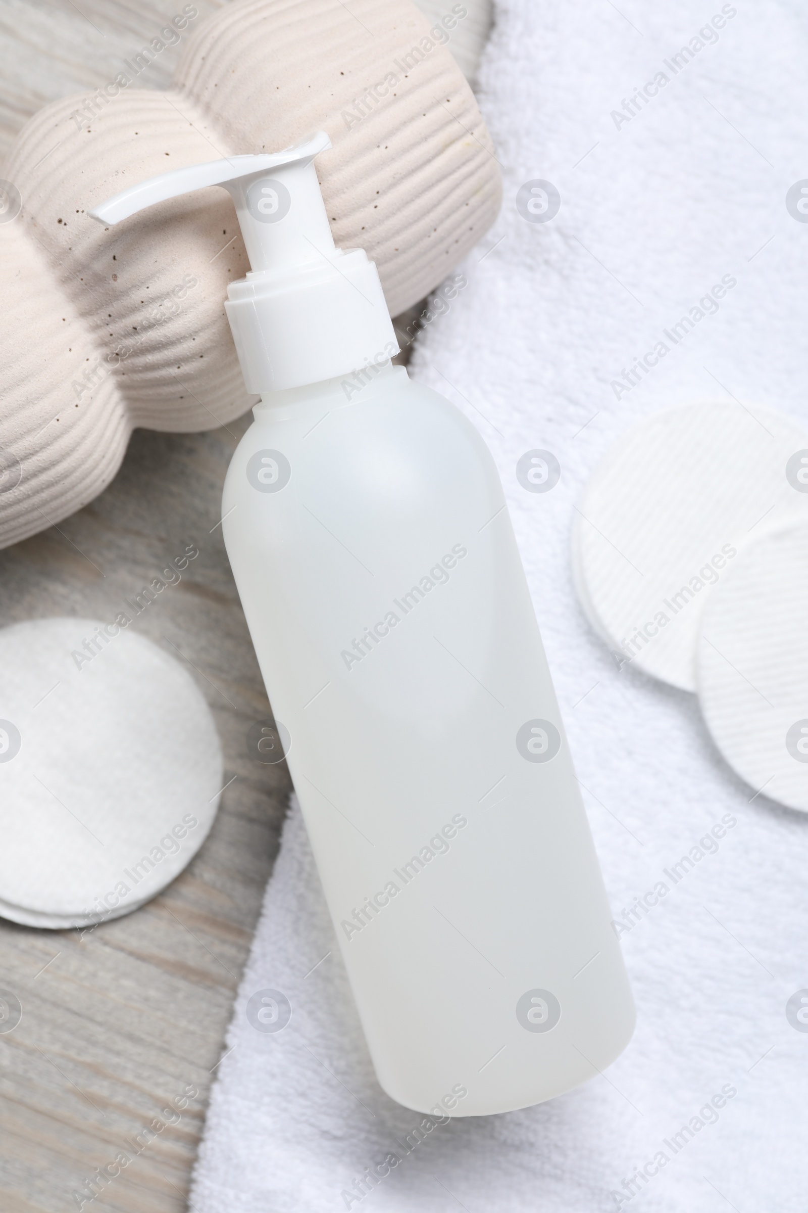 Photo of Bottle of face cleansing product and cotton pads on wooden table, flat lay