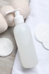 Bottle of face cleansing product and cotton pads on wooden table, flat lay