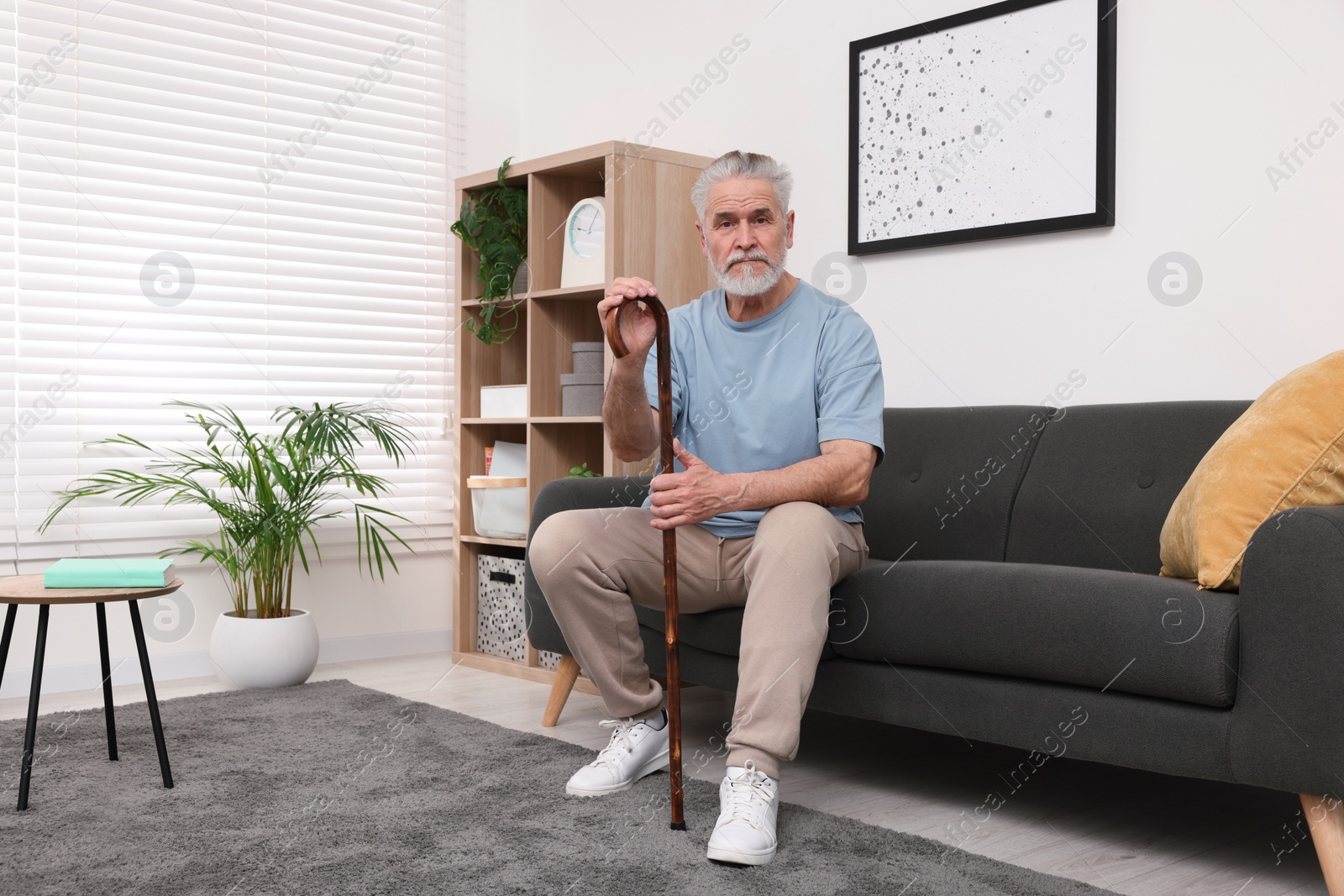 Photo of Senior man with walking cane sitting on sofa at home