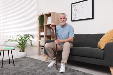 Senior man with walking cane sitting on sofa at home