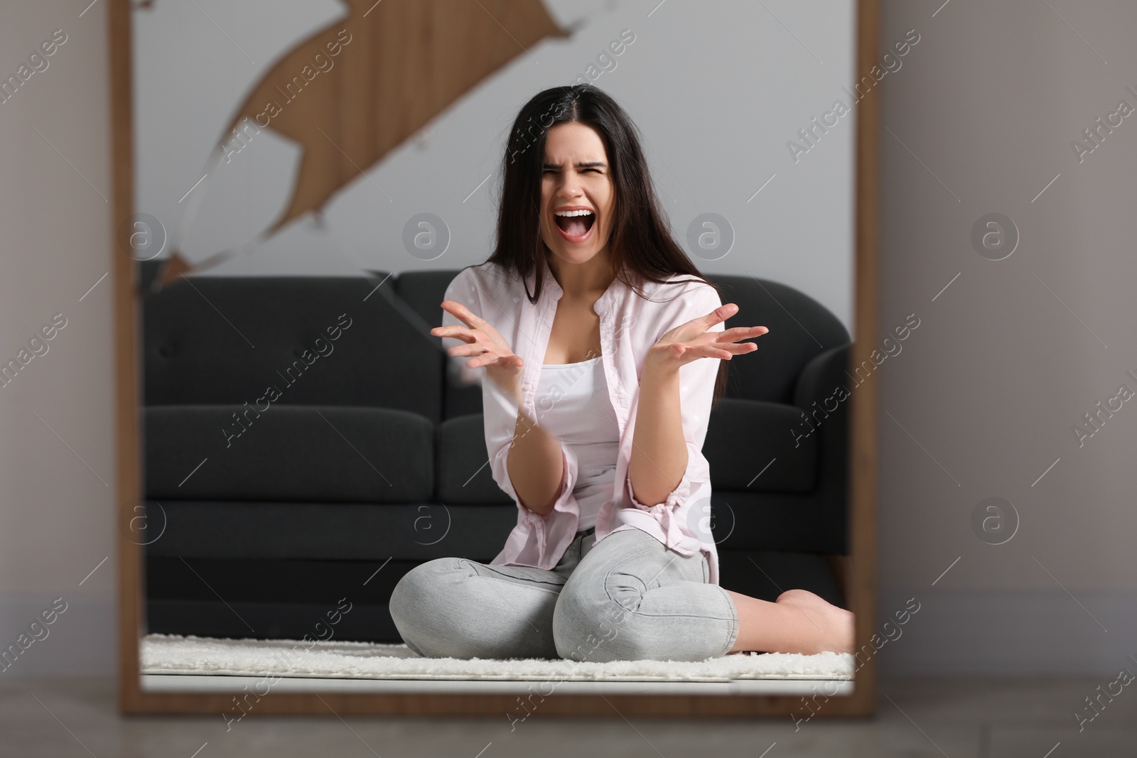 Photo of Mental problems. Woman reflecting in broken mirror while screaming at home