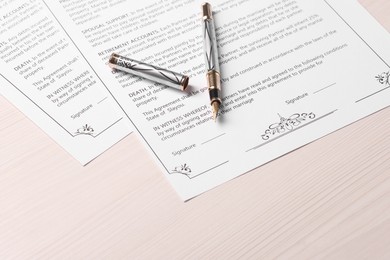 Photo of Marriage contracts and pen on light wooden table
