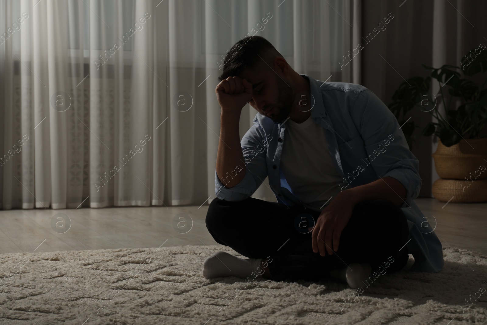 Photo of Sad man sitting on floor near window. Space for text