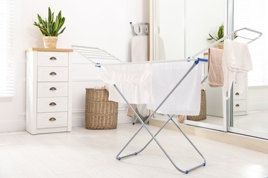 Photo of Clean laundry hanging on drying rack indoors