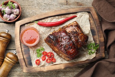 Photo of Piece of baked pork belly served with sauce and chili pepper on wooden table, flat lay