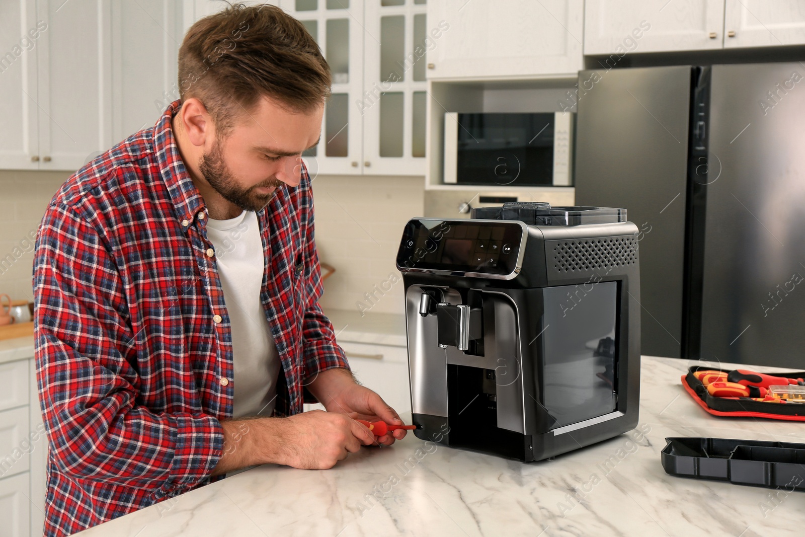 Photo of Man with screwdriver fixing coffee machine at table in kitchen