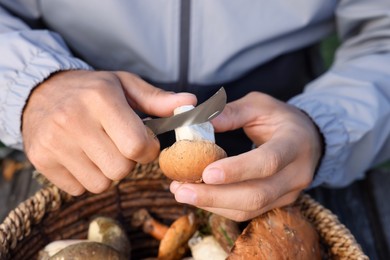 Photo of Man peeling mushroom with knife over basket, closeup