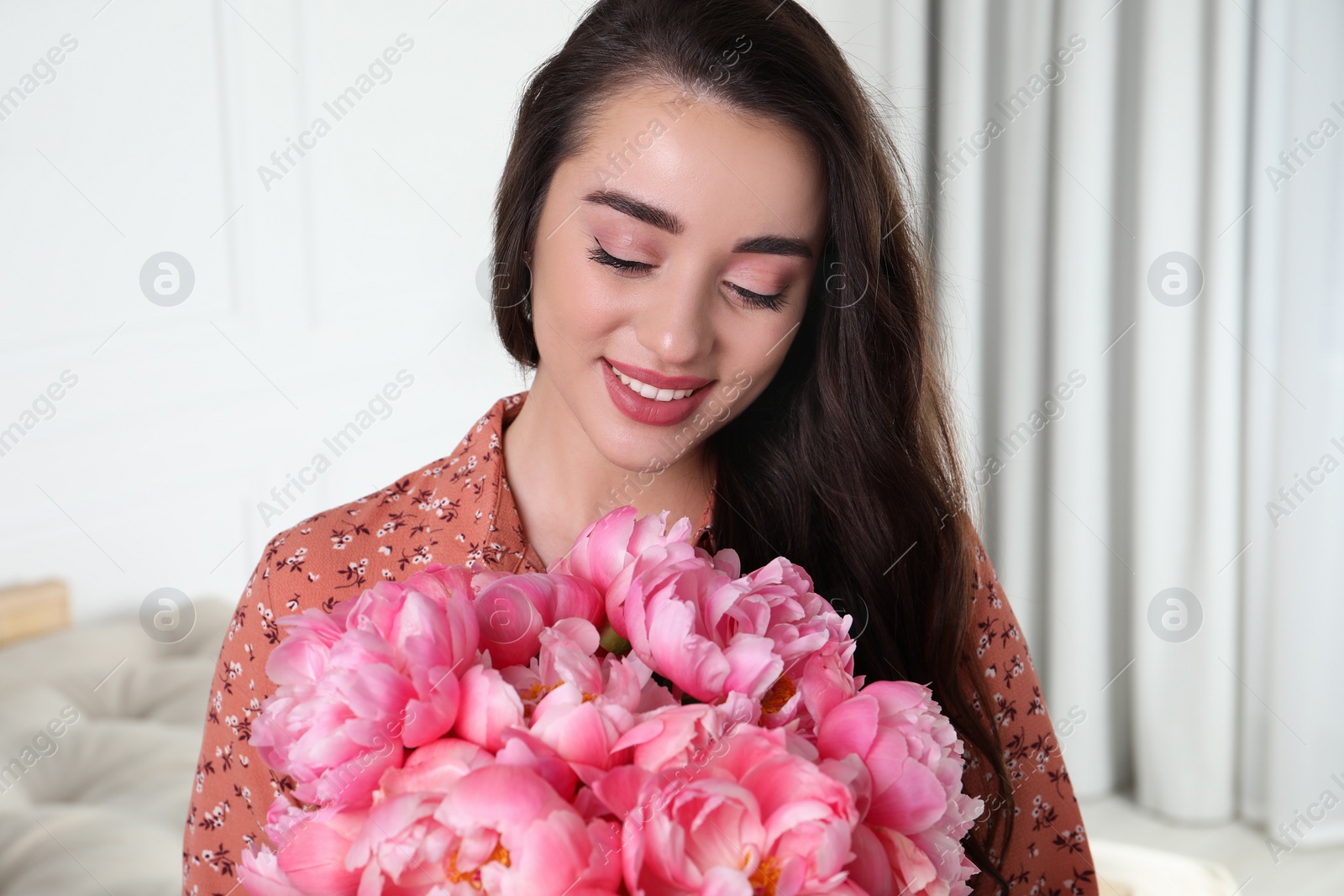 Photo of Beautiful young woman with bouquet of pink peonies at home