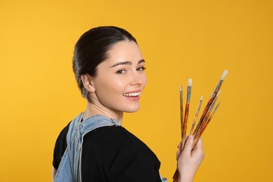 Photo of Woman with paintbrushes on yellow background. Young artist