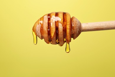 Photo of Delicious honey flowing down from dipper against yellow background, closeup. Space for text
