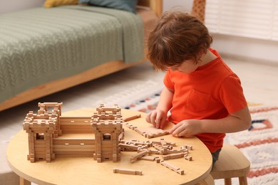 Photo of Little boy playing with wooden construction set at table in room. Child's toy
