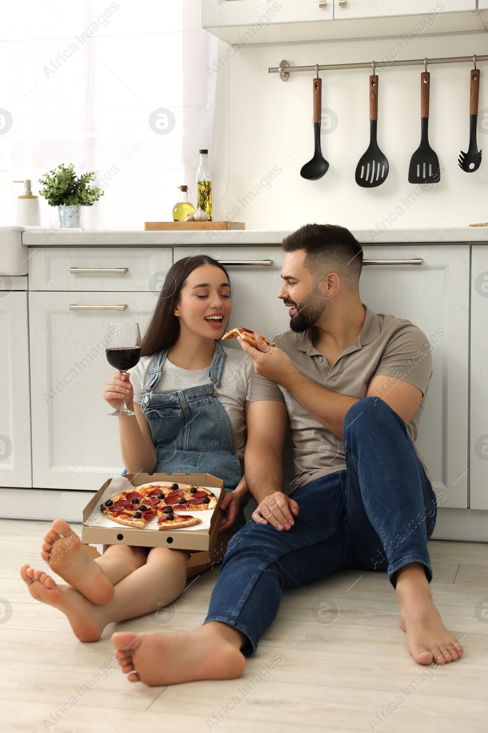 Photo of Happy young couple eating pizza and drinking wine in kitchen