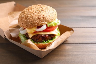 Photo of Delicious burger in cardboard box on wooden table