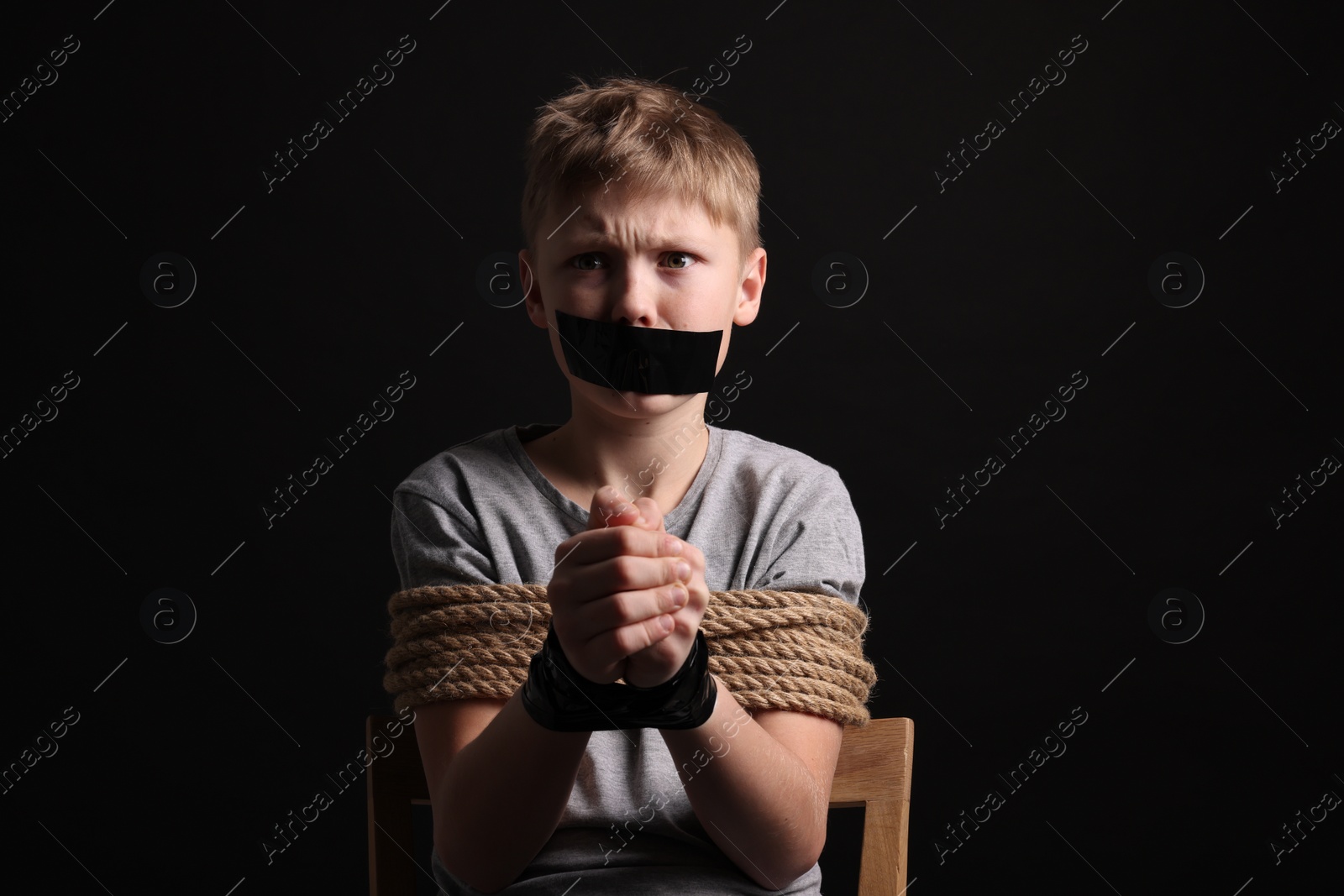 Photo of Little boy with taped mouth tied up and taken hostage against dark background