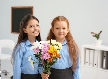 Photo of Happy schoolgirls with bouquet in classroom. Teacher's day