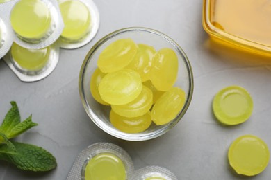 Photo of Many yellow cough drops, honey and mint on light grey background, top view