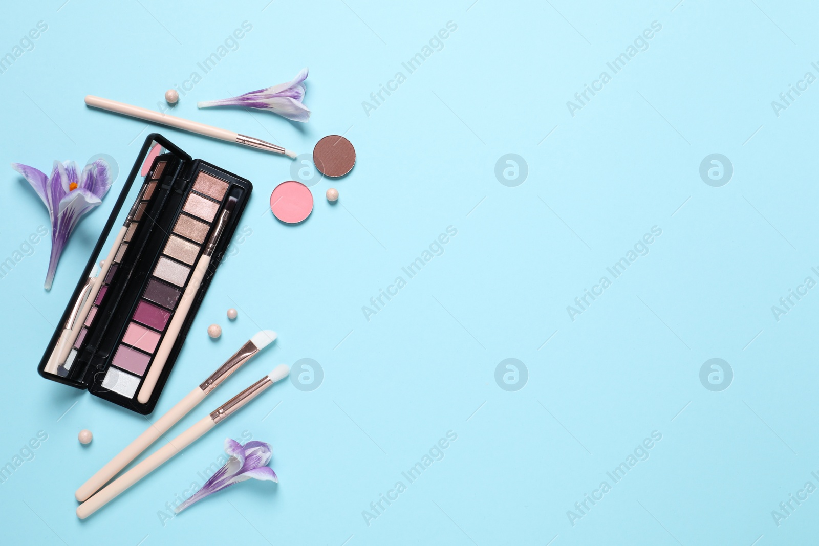 Photo of Flat lay composition with different makeup products and beautiful flowers on light blue background. Space for text