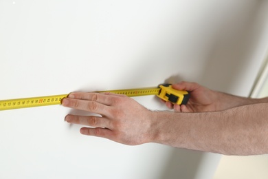 Man measuring white wall indoors, closeup. Construction tool